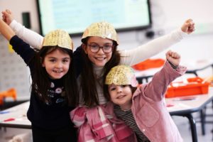 3 young girls wearing brain maps as hats, raising their hands in cheer
