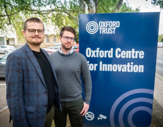 Two men, Thomas Davis (fore) and Jonathan Musgrove (behind) standing in front of Oxford Centre for Innovation totem sign