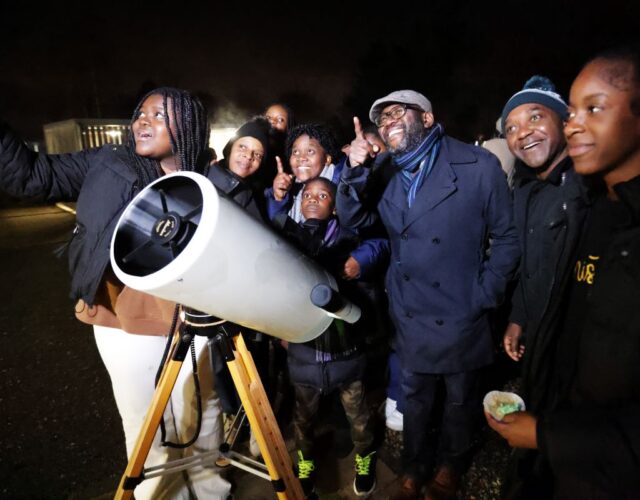 Family with telescope at night pointing at stars in sky