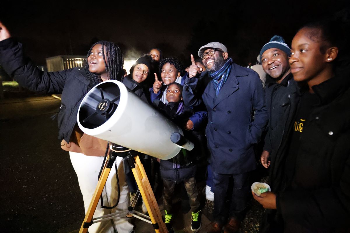 Family with telescope at night pointing at stars in sky