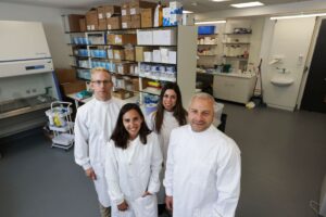 Group of 4 people wearing white lab coats standing in laboratory