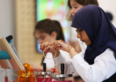 A girl wearing a headscarf and with henna tattoos on her hands hold wires that are part of a science exhibit