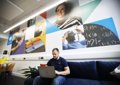 A mat sits on a sofa, working on a laptop within the Barclays Eagle Labs at the Wood Centre for Innovation.