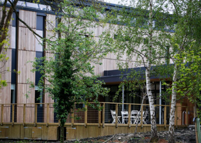 The tables and chairs on the deck area of the Wood Centre Innovation with mature trees in the foreground.