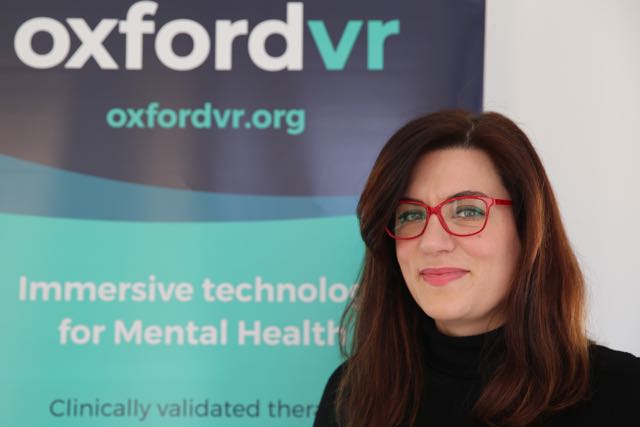 Portrait of Katie Bedborough, COO and CFO of Oxford VR, who stands infront of a branded banner at the Oxford Centre for Innovation.