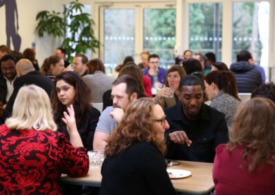 People sit at long tables for a Big Lunch event in the foyer of the Wood Centre for Innovation