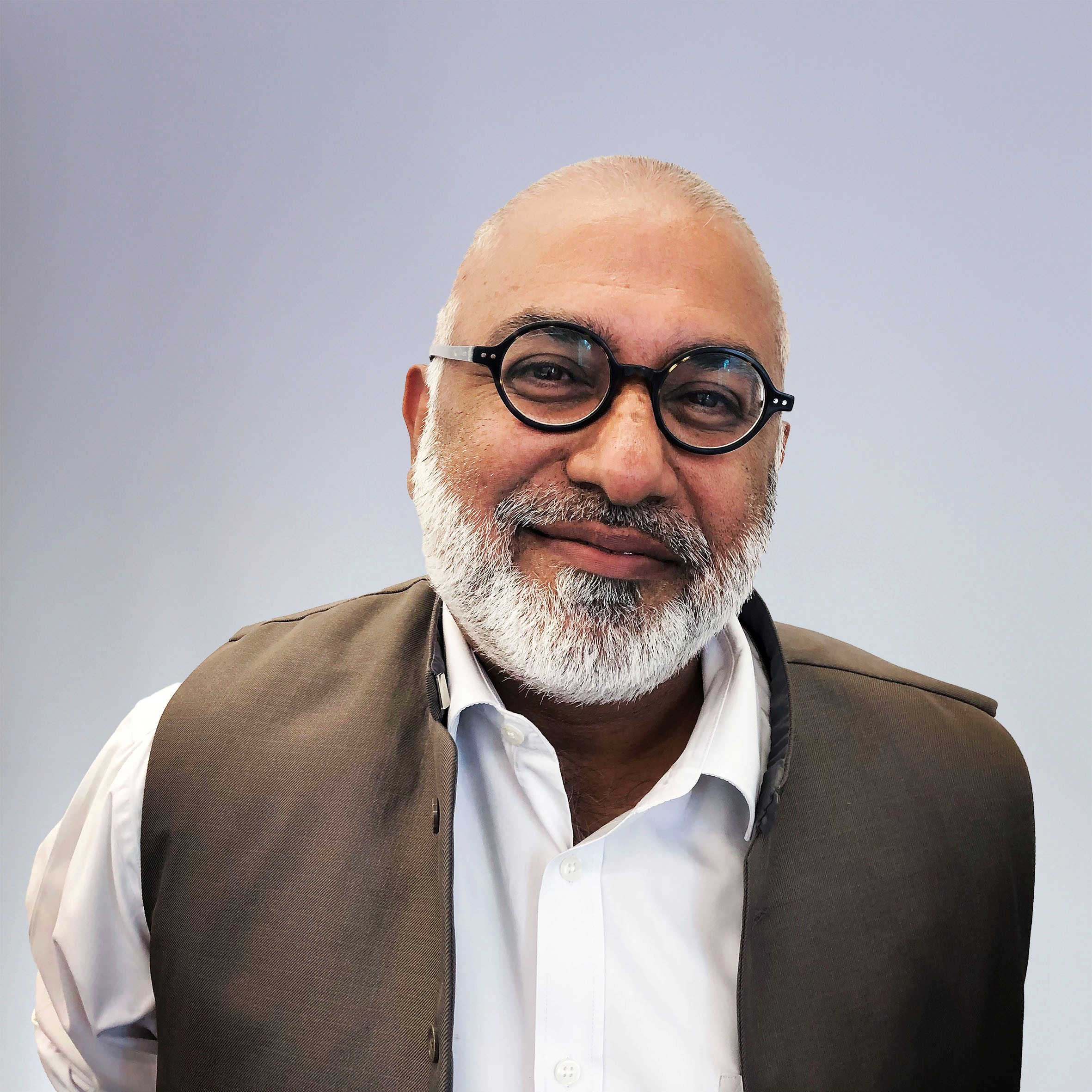 A portrait of Imam Monwar Hussain MBE DL, trustee stands against a white backgroud.