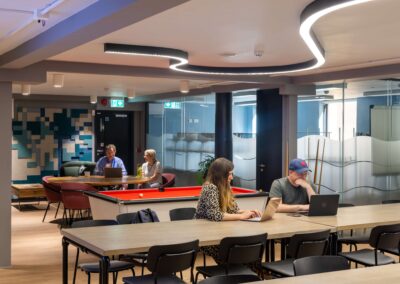 Co-workers sit at long tables working at laptops within the informal meeting area of the Oxford Centre for Innovation.