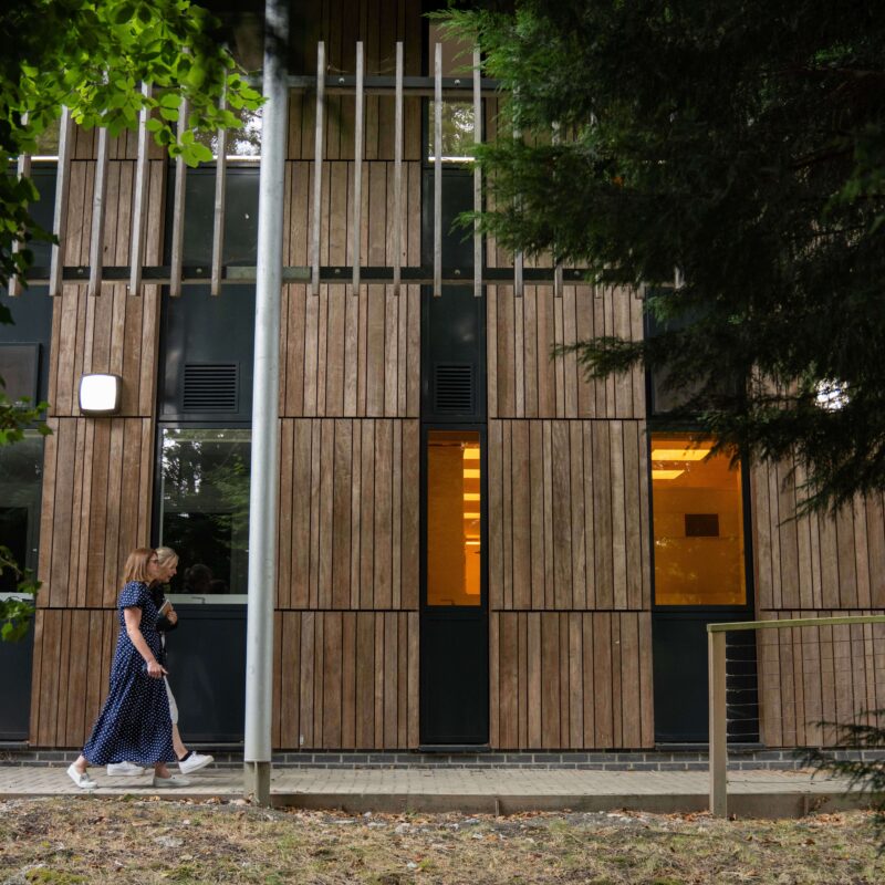 Georgina walking, exterior of Wood Centre People walking outside the Wood Centre for Innovation past the mature trees.