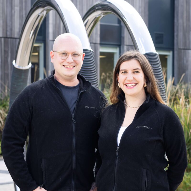 Two people stand outside the Wood Centre for Innovation, smiling, looking at the camera.