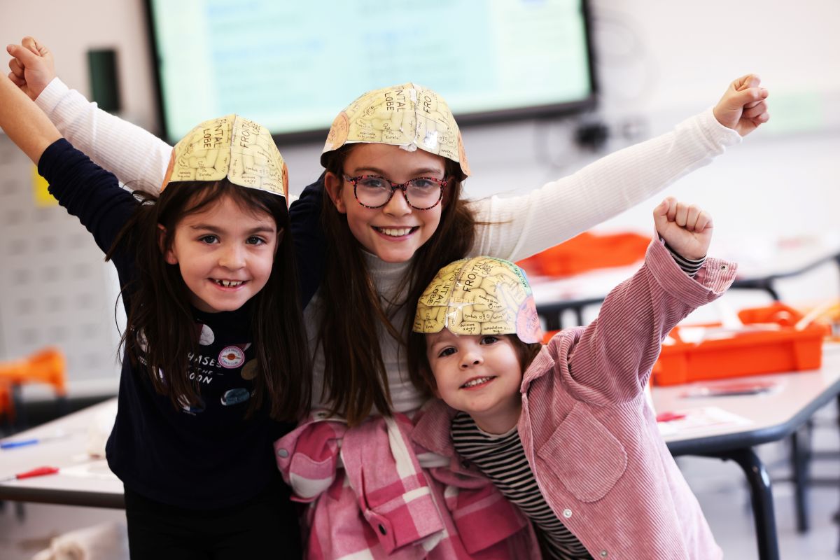 Three girls wearing paper hats with diagram of brain on them